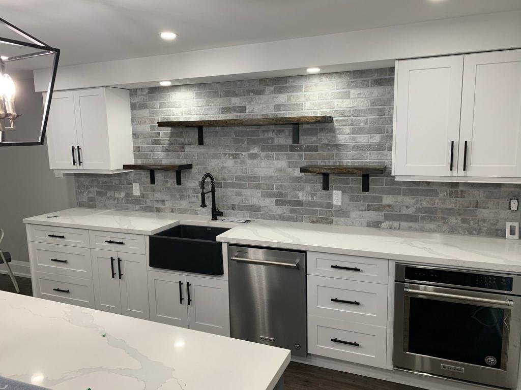 Finished basement kitchen with white cabinets, gray tile backsplash, black sink and stainless appliances