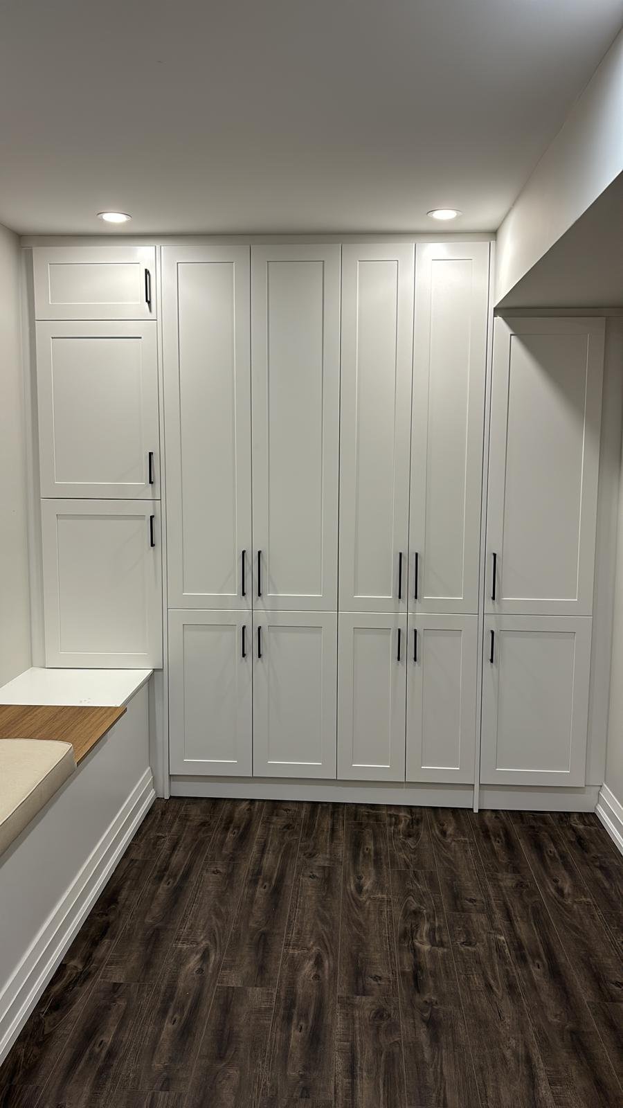 Finished white wall-to-wall cabinets with black handles and a built-in bench