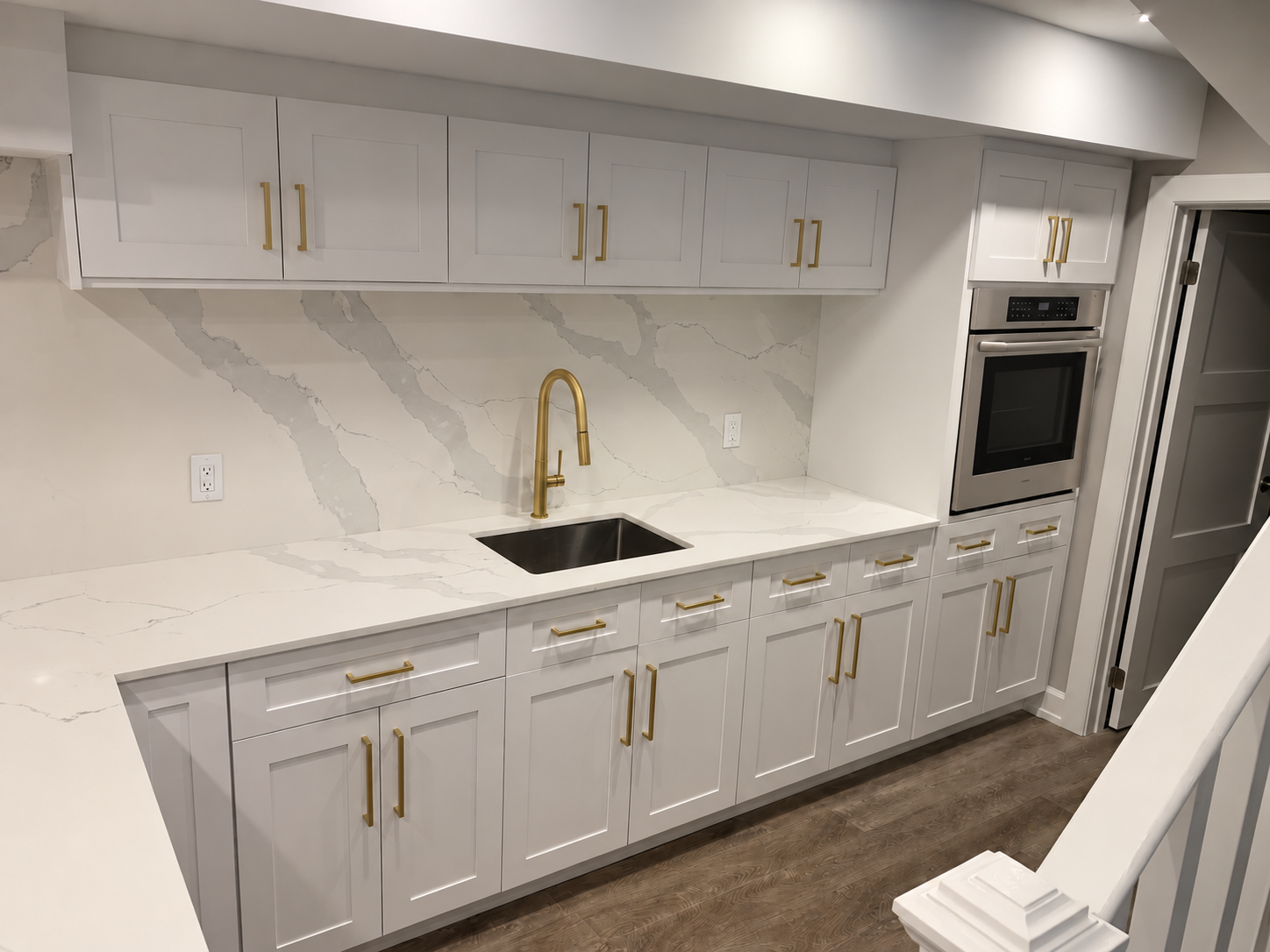 Edited view of white cabinets with gold handles and a built-in wall oven